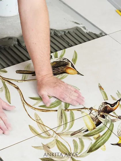 The installation process of custom-printed ceramic tiles. Each tile is a piece of a larger picture, coming together to create a seamless mural of birds perched on olive branches.
