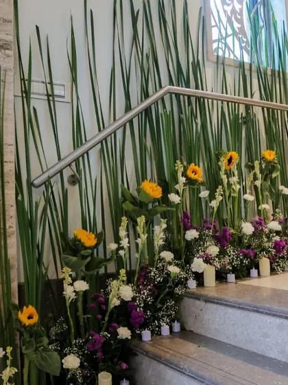 This is a creative way I decorate spaces like stairways. A bed of fresh flowers including sunflowers and purple statice, interspersed with candles, adds a touch of elegance and light to an often-overlooked area.