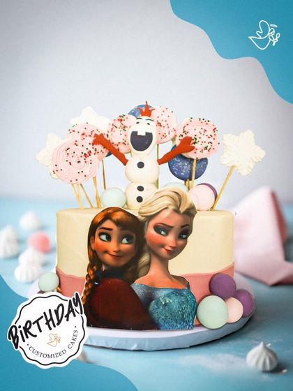 A whimsical Frozen-themed cake featuring Elsa, Anna, and a happy Olaf. The cake is decorated with pink and blue hues, meringue pops, and edible snowflakes for a magical winter wonderland feel.