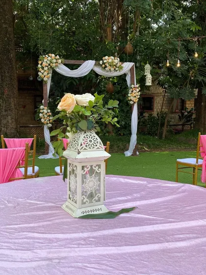 A close-up of a table centerpiece at an outdoor wedding. The decorative white lantern and fresh flowers add a touch of elegance to the guest seating, tying into the overall rustic theme.