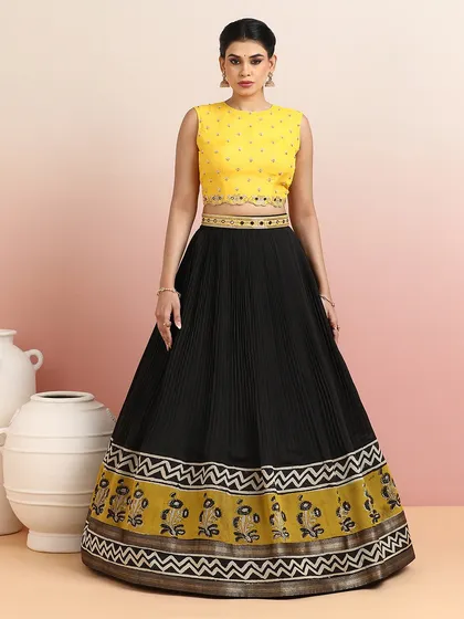A modern classic, this black pleated lehenga is paired with a vibrant yellow embellished blouse. The wide border features a unique floral and zigzag pattern, blending tradition with contemporary design.