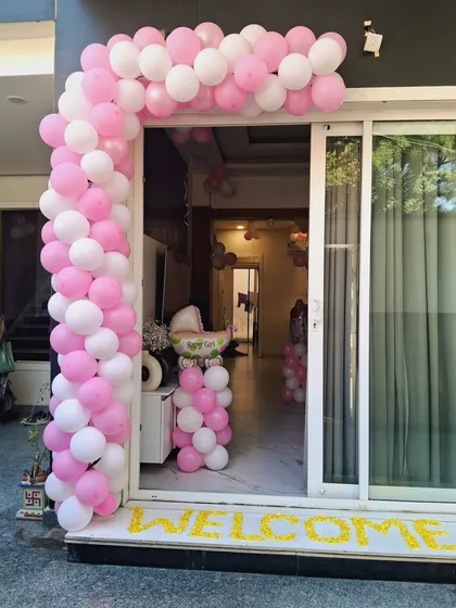 A pink and white balloon arch at the doorway to welcome a new baby home.