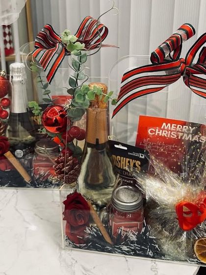 Our beautifully decorated Christmas hampers in clear acrylic boxes. They include sparkling wine, chocolates, and festive ornaments, all tied with a gorgeous striped ribbon.