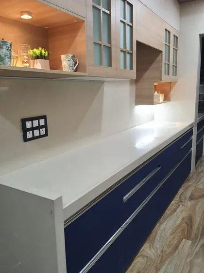 A simple and elegant kitchen with royal blue lower cabinets, a white countertop, and wood-finish upper cabinets with frosted glass.