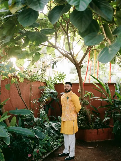 The groom framed by lush greenery, the sunlight creating a beautiful, natural portrait.