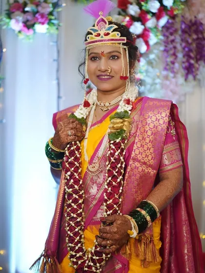 A beautiful photo of a bride during her wedding vidhi. She is wearing a yellow saree with a pink border and the traditional bashinga on her forehead, looking serene and happy.