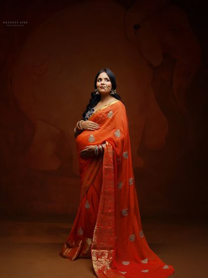A full-length shot showcasing the graceful fall of the saree. This portrait captures the mother-to-be in a moment of quiet contemplation.