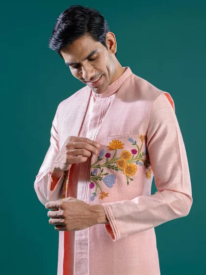 A model adjusts his cuff, showing a hint of the floral embroidery on his pink kurta. This image captures the small, thoughtful details that elevate our ensembles.