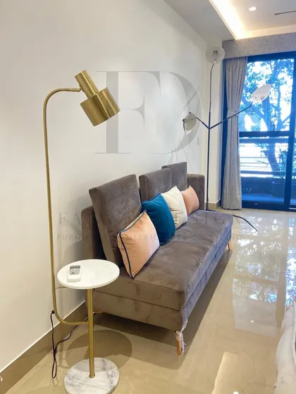 A comfortable sofa-bed in a neutral brown fabric, perfect for a multifunctional space. It's paired with colorful cushions and a modern floor lamp with an integrated marble side table for added utility.