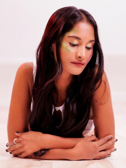 A soft and introspective portrait with artistic glitter makeup. The lighting is gentle, creating a dreamy and ethereal mood.