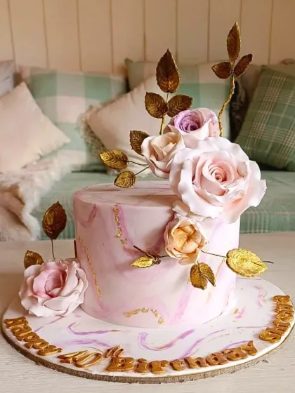 An elegant and modern floral cake with a soft pink marble effect, accented with gold leaf veins and a cascade of handmade sugar roses. This design combines contemporary artistry with timeless romance for a sophisticated celebration.