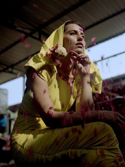 A pensive moment captured during the 'Phool Mandi' shoot. The styling uses a contemporary hooded yellow dress, with falling petals adding a touch of poetic drama to the scene.