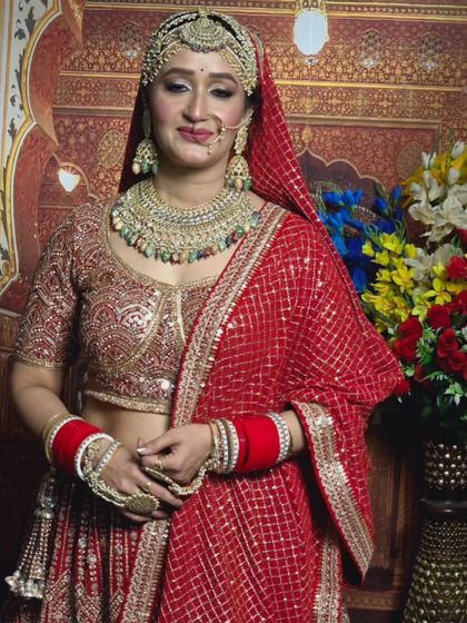 A bride in a red saree-lehenga with golden sequin work, paired with a multi-colored stone jewellery set.
