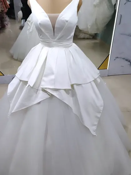 I believe in timeless elegance with a modern twist. This classic white satin ball gown features a structured, layered peplum over a full tulle skirt, creating a powerful and unforgettable bridal silhouette.