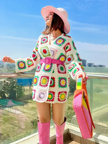 A full-length view of the crochet cardigan styled as a dress. The pink boots and belt tie the whole look together.