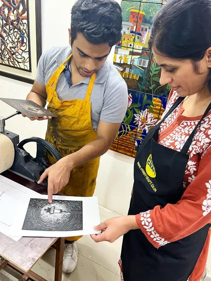 An instructor provides one-on-one guidance, explaining the nuances of a freshly pulled linocut print to a participant.