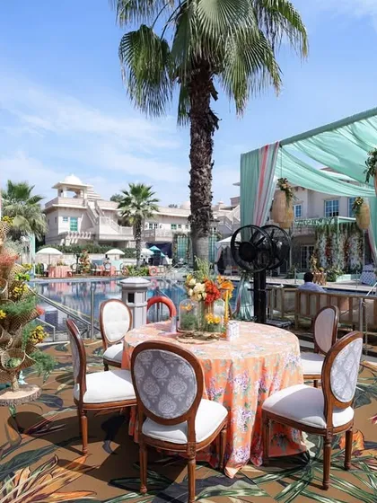 The poolside dining area, with tables covered in orange floral cloths and set on a tropical print carpet, all under a canopy of aqua drapes.