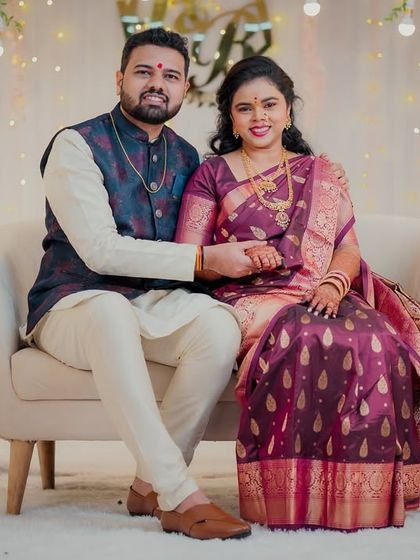 A formal portrait of the engaged couple seated together against a beautifully decorated floral backdrop. They hold hands, smiling for the camera, marking their special day.
