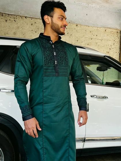 A happy client in a custom-made dark green kurta. This piece features detailed black threadwork on the neckline and cuffs, showcasing our ability to add personalized embroidery to a classic kurta design.