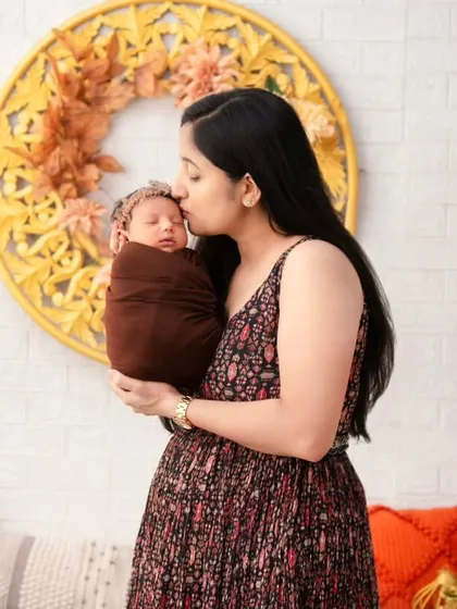 A mother gently kisses the forehead of her sleeping newborn, held lovingly in her arms. This is a portrait of pure maternal love, showcasing the soft, emotional moments we capture in our warm and comfortable studio setting.
