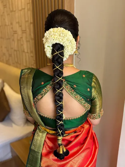 A detailed view of a classic South Indian bridal hairstyle. This intricate braid is woven with gold thread and adorned with fresh jasmine flowers, a style that is both traditional and elegant, designed to hold perfectly throughout the wedding ceremonies.