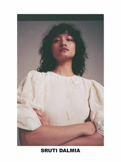 A portrait from the Sruti Dalmia lookbook. The styling is simple and intimate, highlighting the delicate embroidery and puff sleeves of the top, with natural hair and makeup to maintain a soft, authentic feel.