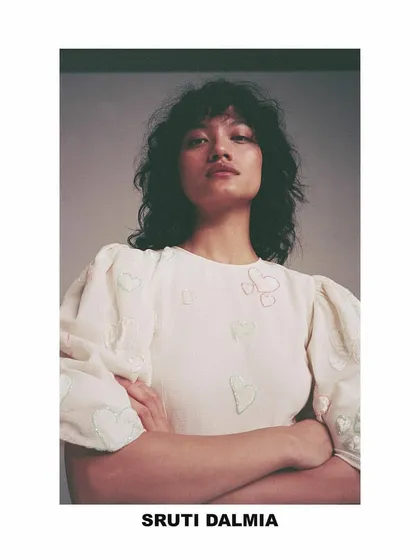 A portrait from the Sruti Dalmia lookbook. The styling is simple and intimate, highlighting the delicate embroidery and puff sleeves of the top, with natural hair and makeup to maintain a soft, authentic feel.