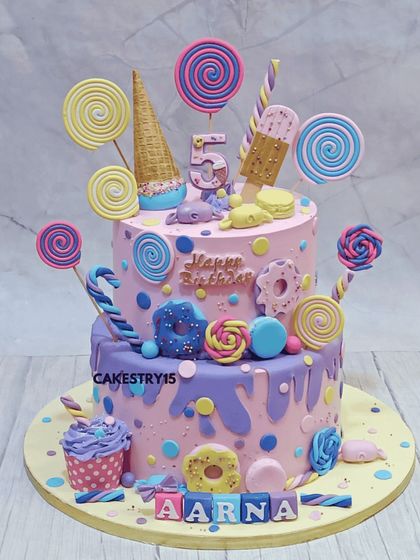 A sweet two-tier Candyland-themed cake for a fifth birthday. This choco-vanilla cake is dripping with fun, adorned with fondant lollipops, donuts, ice cream cones, and a matching cupcake.