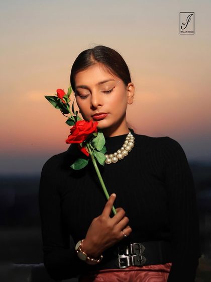A beautiful golden hour portrait. The model holds a single red rose, and the warm sunset tones create a romantic and serene atmosphere.