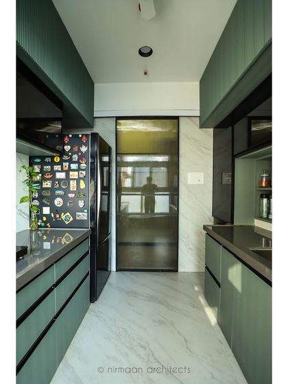 Another view of the sage green kitchen, showing the seamless integration of the refrigerator and the use of a smoked glass door to separate the utility area.
