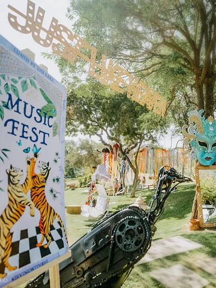 A "Music Fest" welcome sign, featuring tiger illustrations, stands next to a scrap-metal bird sculpture, setting the stage for an event where art and celebration collide.