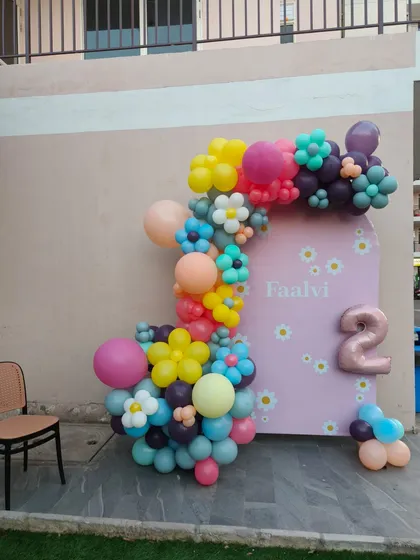 A cheerful daisy-themed second birthday party. This outdoor setup features a pink arched backdrop and colorful balloon flowers.