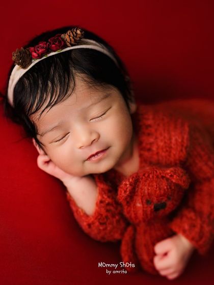 A peaceful newborn in a red knit outfit holding a teddy bear, demonstrating rich color and cozy posing.