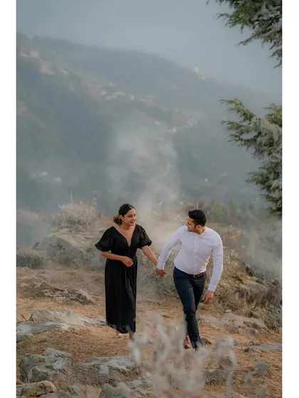 A couple walks hand-in-hand along a misty mountain path, capturing the moody and atmospheric beauty of the Himachali landscape.