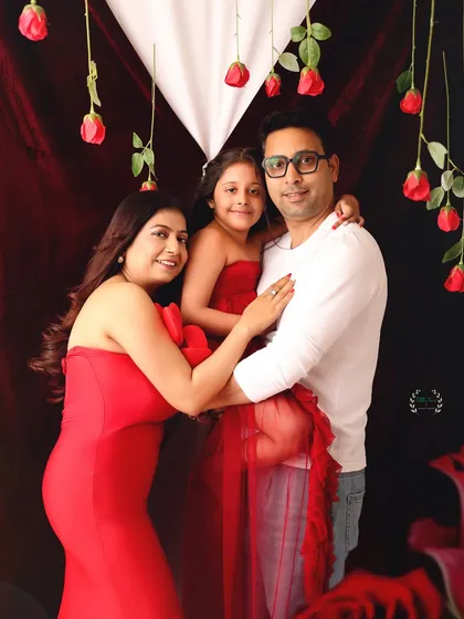 A lovely portrait of a growing family. The daughter sits on her father's lap while he and the expecting mother embrace, showcasing their love and excitement.
