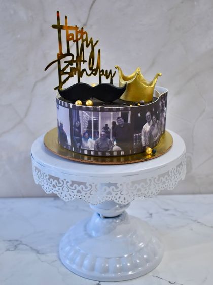 A cake that tells a story through memories. This design features an edible film strip of black and white photos wrapped around the cake, topped with a crown and mustache for a "king's" birthday.