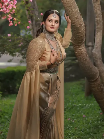 A full-length portrait in a lush green park, showcasing a unique golden gown with a cape. The natural setting enhances the fairytale quality of the outfit.