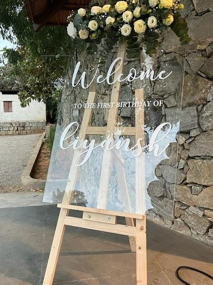 An elegant acrylic welcome sign for Liyansh's first birthday, topped with a beautiful arrangement of white roses.