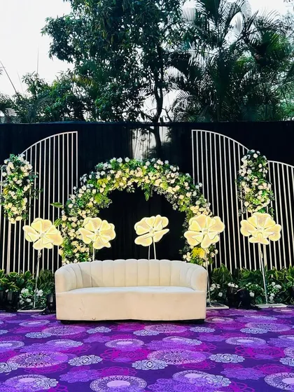 The vibrant purple carpet with traditional motifs adds a layer of richness to this stage design, contrasting beautifully with the white and green floral arrangements.