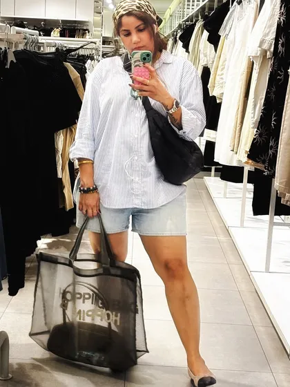 A mirror selfie during a shopping trip, wearing an oversized shirt, denim shorts, and a bandana. This shows a trendy, comfortable look for a day out.