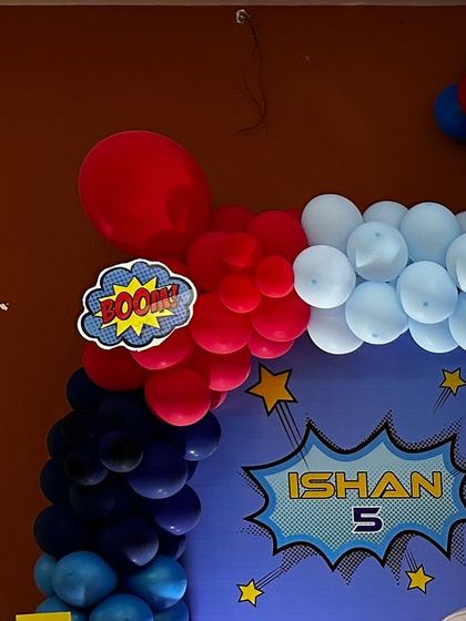 A comic book-style "BOOM!" cutout attached to a red, white, and blue balloon garland for a superhero party. These small details add a lot of character to the setup.