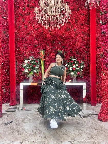 A stunning client looking absolutely beautiful against a wall of red roses. She is wearing our green floral lehenga, perfectly styled for a wedding celebration.