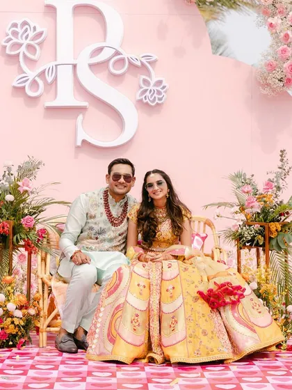 A chic and modern Mehndi or Haldi setup with a personalized monogram on a pink backdrop. The mix of pastel and bright florals gives it a fresh, contemporary feel.