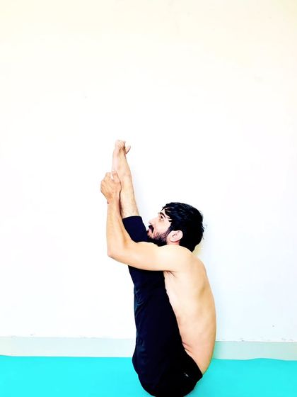 A seated leg-over-head pose, a deep forward bend that requires very open hamstrings and hips.