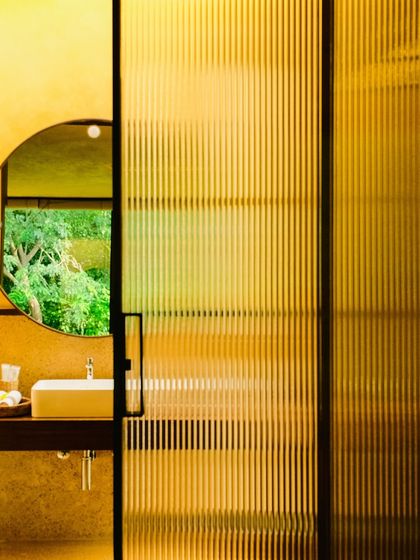 A detail of the bathroom, showing the fluted glass partition and the reflection of the forest, a blend of modern texture and natural beauty.