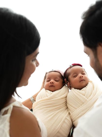 An over-the-shoulder view of parents admiring their swaddled twin babies. This intimate perspective really draws you into their little family bubble.