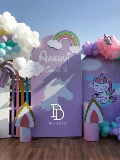 A dreamy unicorn and rainbow themed party for a 3rd birthday. This outdoor setup features pastel rainbow balloon arches, unicorn cutouts, and fluffy balloon clouds, creating a magical atmosphere.