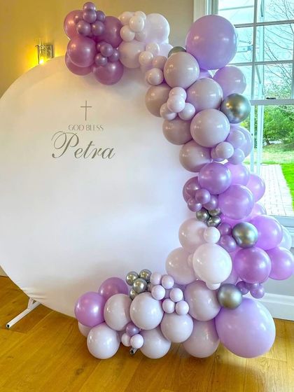 A simple and elegant baptism ceremony decoration. The white circular backdrop is framed by a beautiful purple and silver balloon garland.