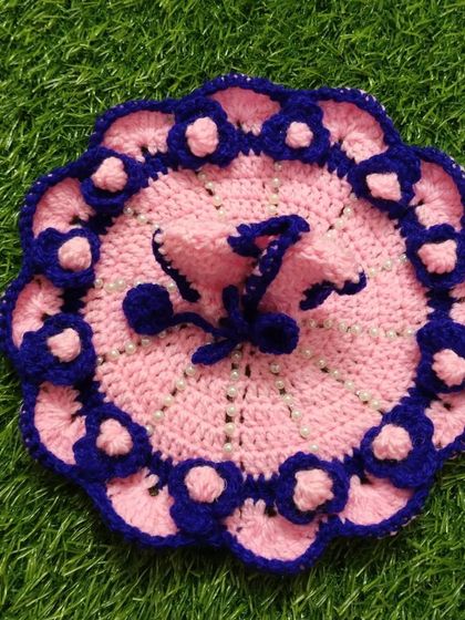 A lovely pink and blue woolen poshak. The base is a soft pink, with a border of dark blue crochet flowers, and the dress is lightly sprinkled with small pearls.