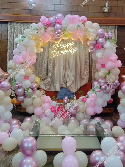 An elaborate balloon ring decoration in pink and white, with added floral touches and balloon pillars for a grand look.